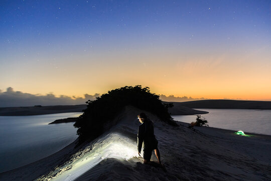 Homem com lanterna de cabe&ccedil;a observando o amanhecer em acampamento nos Len&ccedil;&oacute;is Maranhenses