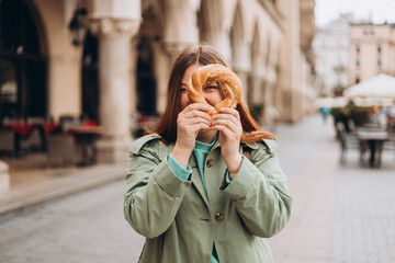 Attractive young female tourist is holding prezel, traditional polish snack on the Market square in Krakow. Traveling Europe in spring. Selective focus. High quality photo
