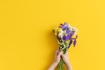 bouquet of flowers in children’s hands on yellow background . Backdrop greeting for Mother’s Day.