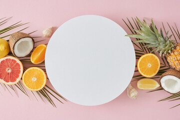 Juicy summer concept. Top view flat lay of orange lemon slices, grapefruit, coconut, pineapple, palm leaves and seashells on pastel pink background with blank circle for text or advert