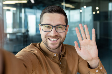 Successful young businessman talking with friends on video call, man smiling and waving at...