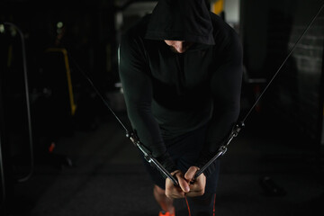 Strong male bodybuilder in black hood doing exercises in the gym