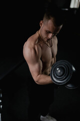 Fototapeta na wymiar A strong male bodybuilder shakes his biceps in the gym with a barbell and dumbbells, at this time the muscles are tense