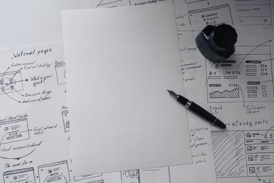 Blank sheet of paper and a pen on background with wireframes of IT project. User experience design layout, creative ideas for new project. Brainstorming.