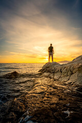 Fototapeta premium Young man standing on rocky beach at sunset time 