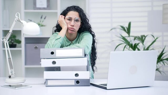 Young employee tired and exhausted by paperwork accountant manager or agent sits leaning on a stack of folders unfinished documents from large pile of office papers Stress at work, overworked female
