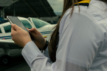 Female Pilot Checking Phone While Parked Plane in Background