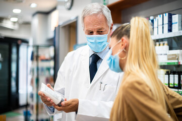 Senior pharmacist dealing with a customer, both of them wearing masks due to coronavirus
