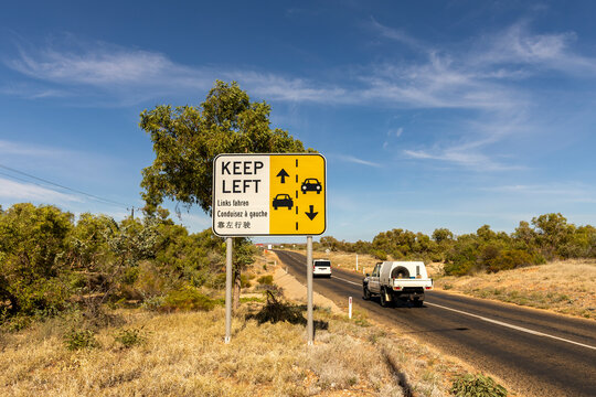 street sign "keep left" written in English, German, French and Chinese besides a asphalt road in Australia and two cars passing by, travel australia