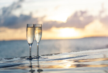 Two glasses of champagne on the side of the infinity pool against the backdrop of a sunset in the Maldives - obrazy, fototapety, plakaty