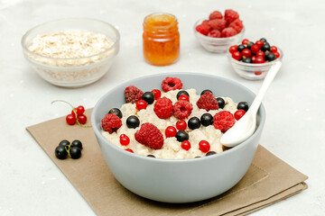 Oatmeal porridge with summer raspberry, currant berries,honey. Porridge oats in bowl with fruits. Healthy food breakfast,lifestyle,dieting, proper nutrition.Top view flat lay on gray table background