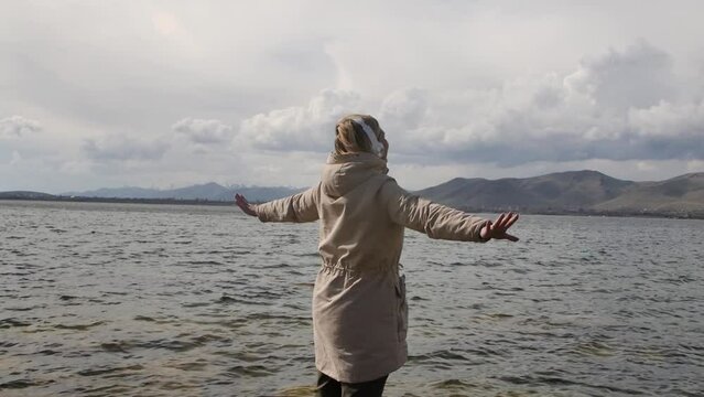 An adult Caucasian blonde standing on the seashore and spreading her arms to the sides like a bird enjoys nature and the sound of music using headphones. Happy people. Woman enjoying life
