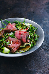 Traditional Commonwealth Sunday roast as sliced cold cuts roast beef with zucchini and onion rings in in rocket lettuce served as top view on a design bowl