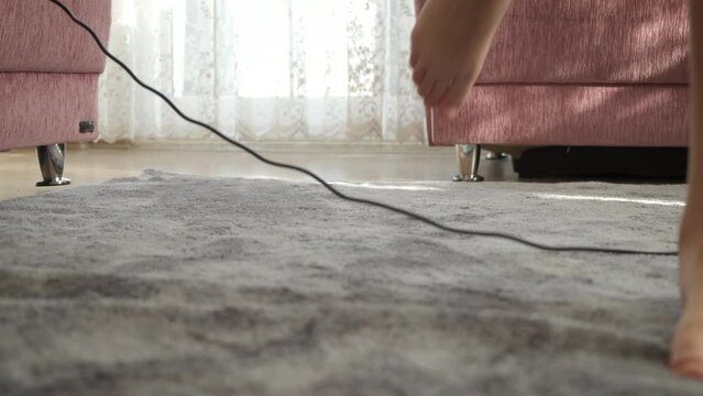 Stumbles by wire in room. A little girl stumbles by a wire on the carpet on the floor in the room.