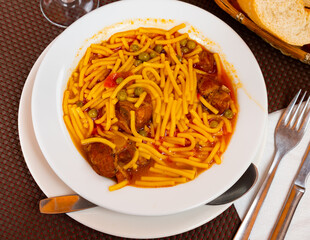 Flavored soup containing beef, noodles and green peas in a bowl
