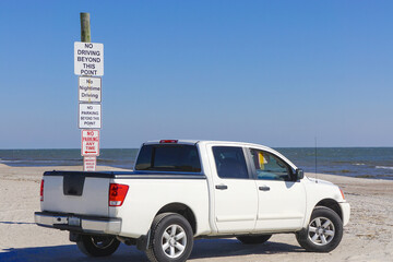 Fernandina Beach, Florida: A pick-up truck is parked on the sand at Fernandina Beach beach next to a pole with a stack of signs warning of local regulations. © Linda Harms