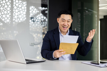 Businessman at work, Asian man reading a good letter from the bank about opening a credit line, the boss is pleased and celebrating the success of the company's finances.