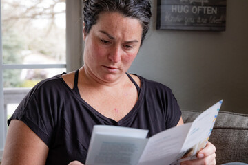 Close-up horizontal image of young 30s female reading skin cancer literature on couch at home upon...