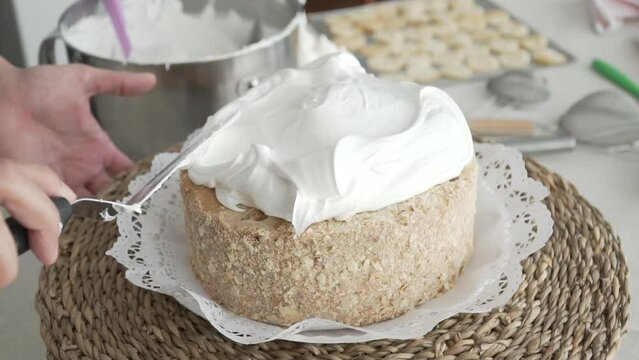 Slow motion of pastry chef's hand spreading meringue with long spatula. Sheet cake on rotary base