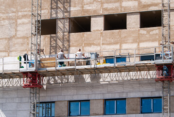 Dos albañiles trabajando en la fachada de un edificio en construcción, desde un andamio.
