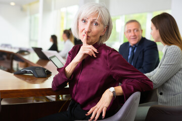 Elegantly dressed senior white businesswoman sitting at conference table during corporate meeting...