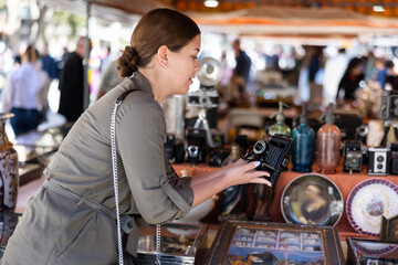Smiling female tourist checking out old camera at flea market