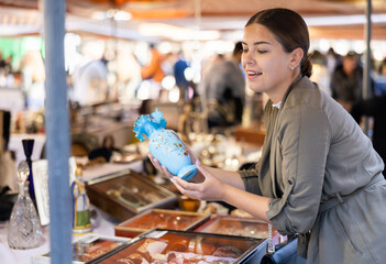 Smiling female tourist checking out nice ceramic vase at flea market