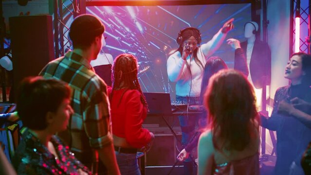 Happy people attending disco party, dancing and having fun on dace floor at club. Young men and women jumping on electronic music at celebration event, discolights. Handheld shot.