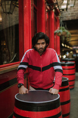 Fashion portrait of Indian Guy on the front of old building looking to the camera wearing a red shirt. Indian lifestyle and fashion