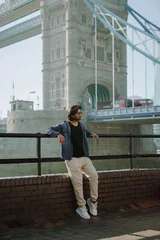 Foto op Plexiglas Handsome stylish guy from India in London is opposite of London Bridge.London Bridge and London red bus. © Myroslava