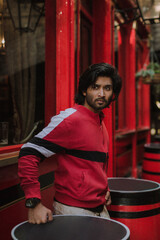 Obraz na płótnie Canvas Fashion portrait of Indian Guy on the front of old building looking upside wearing a red shirt. Indian lifestyle and fashion