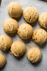 Scoops of vanilla cookie dough on a parchment lined cookie sheet, plain vanilla cookie dough about to be baked