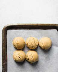 Scoops of vanilla cookie dough on a parchment lined cookie sheet, plain vanilla cookie dough about to be baked