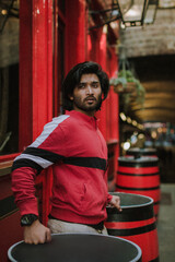 Fototapeta na wymiar Fashion portrait of Indian Guy on the front of old building looking upside wearing a red shirt. Indian lifestyle and fashion