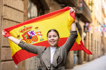 Patriotic young woman waving the flag of Spain on the city street