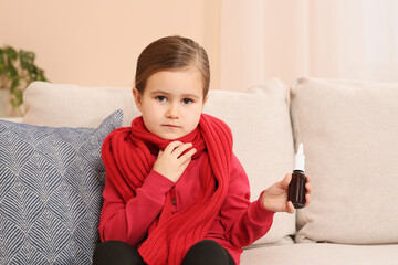 Cute little girl holding nasal spray on sofa at home