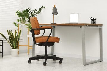 Stylish office interior with comfortable chair, desk, laptop and houseplants