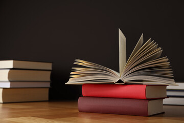 Many books stacked on wooden table near black wall, space for text