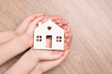 Home security concept. Woman and her little child holding house model at wooden table, top view with space for text