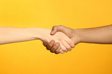 International relationships. People shaking hands on orange background, closeup