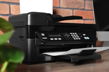 Modern printer with paper near computer on wooden desk at home