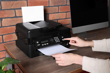 Woman using modern printer at wooden desk in home, closeup