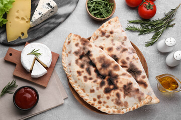 Tasty pizza calzones with tomato sauce and different products on light grey table, flat lay