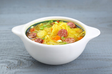 Delicious sauerkraut soup with smoked sausages and green onion on grey wooden table