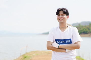 Handsome Asian volunteer smiling to camera portrait, man pointing finger at his volunteer t-shirt. Happy cheerful male volunteer proudly smiles to camera while working.