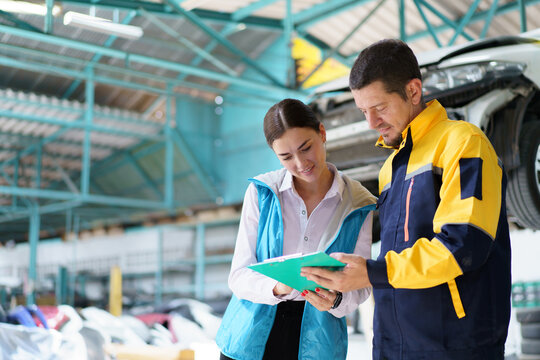 Caucasian white young woman taking her car to garage to have an annual check up and talking or discussing to technician. 