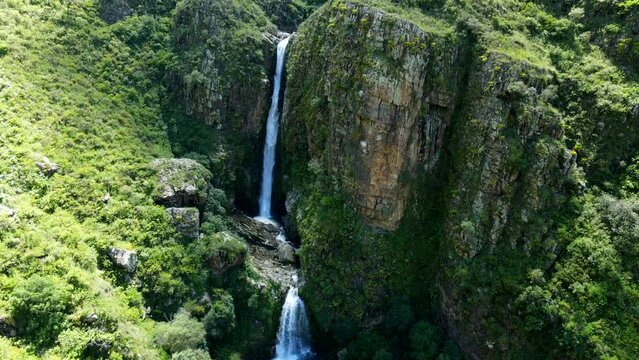 Aerial shot drone ascends while camera pans down over double waterfall in mountainous green forest