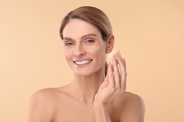 Obraz na płótnie Canvas Woman blending foundation on face with makeup sponge against beige background
