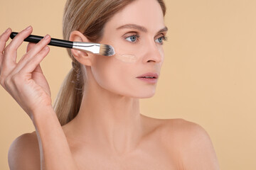 Obraz na płótnie Canvas Woman applying foundation on face with brush against beige background
