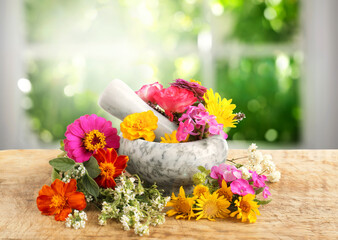 Marble mortar and different flowers on wooden table in room